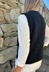 Chaleco tejido de punto color negro, con escote en V y cierre frontal de tres botones grandes de madera. Presenta un diseño clásico y versátil.
