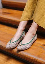 Bailarina de rejilla bordada con diseño de flores pequeñas en tonos beige y amarillo, con ribetes y talón en ante color verde. Presenta un detalle de media esfera metálica dorada en la puntera y suela plana.