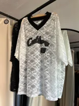 Remerón de encaje negro con diseño de cuello en V y mangas cortas. Presenta un estampado frontal bordado con texto y el número 32.