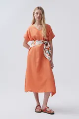 Vestido midi color naranja de lino, con escote en V, mangas cortas con dobladillo, bolsillos laterales y tajos laterales. Incluye un pañuelo estampado atado a la cintura.