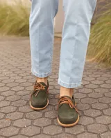 Zapatos náuticos de cuero verde oscuro, estilo mocasín con cordones de cuero marrón claro, costuras visibles en contraste y suela plana.