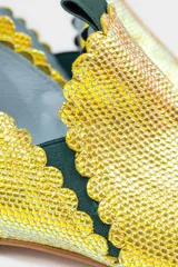Botín de piel tornasolada con acabado brillante en tono amarillo lima y reflejos verdes. Presenta un diseño de dos piezas con bordes troquelados, aberturas laterales, ajuste con elásticos y un borlón decorativo de ante verde en la parte trasera. Incluye cuña interna y suela de cuero.