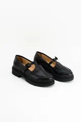 Mocasines estilo Mary Jane con diseño de estampado de vaca (cow print), confeccionados en cuero. Presentan una tira con hebilla ajustable sobre el empeine y una suela track negra de 4,5 cm de altura.