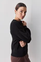 Sweater negro de tejido suave con escote redondo, mangas largas y calce relajado, con terminaciones acanaladas en cuello, puños y ruedo.