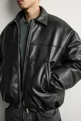 Cazadora acolchada relaxed fit de efecto piel en color negro, con cuello camisero, cierre frontal de cremallera metálica, bolsillos frontales de vivo y puños elásticos.