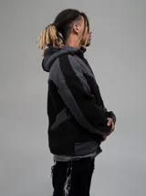 Campera con capucha confeccionada en tejido tipo polar, con diseño de bloques de color en tonos negro y gris oscuro. Presenta cierre frontal completo y ajuste regular.