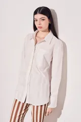 Camisa blanca oversize de algodón, con cuello clásico, cierre frontal con botones de nácar y bolsillo en el pecho.