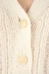 Cardigan de punto color marfil con cuello en V, cierre frontal de botones y mangas largas abullonadas. Presenta un diseño de tejido con textura vertical y corte corto.