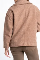 Campera de abrigo color crema, con cuello solapa y cierre asimétrico frontal. Presenta textura bouclé o de lana rizada.