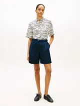 Camisa de manga corta Tommy Hilfiger de corte amplio y hombros ligeramente caídos, confeccionada en puro lino blanco con estampado geométrico de líneas azules. Cuenta con cuello inglés, cierre frontal de botones, bolsillo de parche en el pecho y logo bordado.