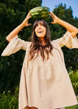 Vestido corto color beige, de lino y corte en A, con escote en V con tiras para anudar y mangas amplias.