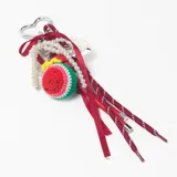 Llavero decorativo con mosquetón metálico en forma de corazón, que incluye una variedad de elementos colgantes: una pieza tejida a crochet con forma de sandía, una tira de perlas, cintas de raso rojas y cordones deportivos con punteras metálicas.