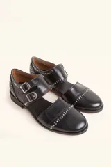 Zapato tipo oxford abierto en los laterales, confeccionado en cuero vacuno negro. Presenta doble tira con hebillas metálicas en el empeine y detalle de tachas plateadas en el contorno del talón y la puntera.