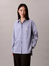 Camisa Calvin Klein de corte regular, con diseño de rayas verticales en tonos azul y blanco. Cuenta con cuello camisero, cierre frontal de botones, mangas largas y un bolsillo aplicado en el pecho con el logo bordado de la marca.