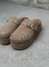 Zuecos color beige de gamuza con detalle de tachas y hebilla metálica.