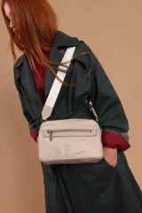 Bandolera de diseño moderno y funcional, confeccionada en nylon color marrón claro. Cuenta con múltiples compartimentos con cierre metálico, herrajes plateados y una correa ancha ajustable con detalle de marca.