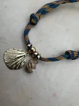 Gargantilla con cordón doble en tonos naranja y gris, con dije de concha dorada y dije de caracol blanco.