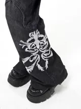 Jean de corte oxford y tiro bajo, color negro con efecto lavado. Presenta estampa bordada en la parte inferior de una de las piernas y detalles de costuras reforzadas en las rodillas.