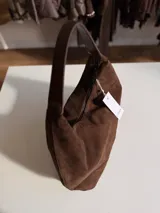 Cartera tipo hobo de diseño relajado, confeccionada en material con textura simil gamuza color chocolate. Presenta una silueta suave, cierre superior y asa corta combinada en simil cuero al tono.