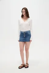 Minifalda de jean azul con cierre frontal de botones metálicos y detalles de estampado animal print en la pretina y los bolsillos superiores. Cuenta con un dobladillo desmechado.