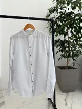 Camisa blanca con finas rayas azules, cuello mao y cierre frontal con botones marrones de efecto madera, de manga larga.