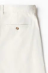 Pantalón chino de sarga elástica de algodón, con cierre de cremallera y botón, bolsillos laterales al bies y bolsillos traseros con botón. Presenta un corte ajustado que define la silueta.