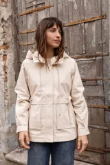 Gabardina liviana color beige con capucha, cierre frontal oculto y cintura ajustable mediante cordón. Presenta bolsillos delanteros amplios y mangas largas con puños rectos.