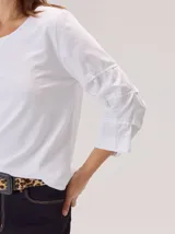 Remera de algodón color blanco, con cuello redondo y mangas tres cuartos con volados escalonados y detalles de pespuntes.