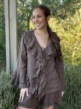 Camisa de lino azul marino con volados en cascada a lo largo del frente y en los puños de las mangas largas. Presenta un escote en V con un botón de nácar visible.