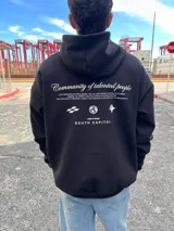 Canguro negro con capucha, de corte holgado y manga larga. Presenta un estampado gráfico en la espalda con el texto 'Community of talented people' y 'SOUTH CAPITAL' junto a iconos minimalistas.