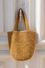 Bolso tipo tote color camel, confeccionado en material trenzado con textura rústica, doble asa de hombro y pequeño aplique metálico con el logo de la marca.