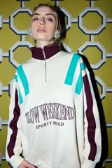 Buzo color crema con cuello alto y cierre frontal parcial. Presenta bloques de color en turquesa y bordó en los hombros y mangas, y un estampado frontal con la frase "SLOW WEEKEND SPORTY MOOD" en bordó.