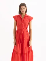 Vestido camisero largo color rojo, de mangas cortas con hombros estructurados y falda escalonada con volados. Presenta cierre frontal con botones y lazo ajustable en la cintura del mismo material.