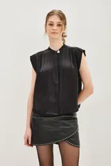Camisa sin mangas de satén negro, con cuello mao y cierre frontal oculto con un botón decorativo en forma de corazón en la parte superior. Presenta un corte recto y fluido.