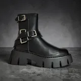 Borcego de caña media color negro, con suela track de plataforma alta y diseño de múltiples correas con hebillas metálicas plateadas en la parte superior y el tobillo.