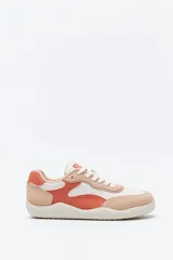 Zapatilla urbana de perfil bajo con diseño barefoot, confeccionada con paneles combinados en tonos blanco, naranja y beige. Presenta suela flexible con textura grabada y cierre mediante cordones.