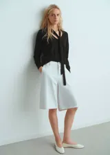 Jersey de punto fino color negro, con cuello en pico y detalle de fular integrado en el escote. Presenta un diseño recto y mangas largas.