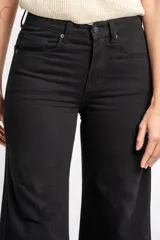 Jean de corte wide leg y tiro medio, confeccionado en algodón peinado de color negro. Presenta un diseño de pierna ancha con ruedo deshilachado y cierre frontal con botón y cremallera.