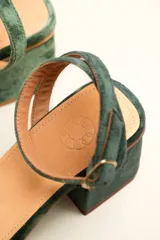 Sandalia de tacón cuadrado medio, confeccionada en terciopelo negro. Presenta un diseño de tiras cruzadas con nudo en la parte delantera y una tira ajustable con hebilla en el tobillo.