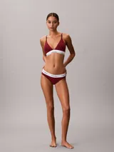 Bralette Calvin Klein de corte triangular, confeccionado en mezcla de algodón elástico y modal, con estampado gráfico en tonos rojos y banda elástica inferior en color blanco con el nombre de la marca en contraste.