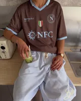 Camiseta de fútbol color marrón con cuello en V y detalles en celeste, inspirada en el Napoli F.C., con diseño de mangas cortas y sponsors impresos en el frente.