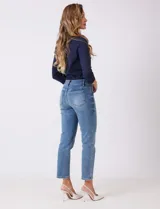 Jean azul de calce semi-ajustado, estilo Mom Slim, de tiro alto, relajado en la cadera y muslos, con pierna que se angosta levemente hacia el tobillo. Tiene pretina clásica con pasadores para cinturón, cierre frontal con cremallera y botón metálico, y bolsillos delanteros y traseros.