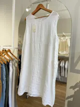 Vestido corto blanco de lino, sin mangas, con cuello redondo y bolsillos laterales. Tiene cierre con botones en la espalda.