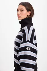 Campera de punto holgada con cuello tipo chomba y cierre frontal oculto. Presenta un diseño de rayas horizontales en tonos marrón, rojo y crema, con puños y ruedo acanalados. Incluye un parche bordado en la manga izquierda.