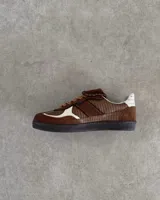 Championes de cuero vacuno con diseño de paneles en tonos marrones y detalles en blanco. Presentan una combinación de texturas lisas y grabadas, con cordones planos y costuras decorativas en la lengüeta.