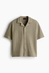 Camisa color caqui de manga corta con cuello resort y tapeta con botones. Tejido de punto waffle con corte holgado.