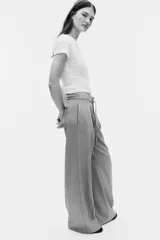 Pantalón sastre de tiro alto, color gris, con cordón ajustable en la cintura, piernas amplias con pinzas, raya marcada, bolsillos laterales discretos y bolsillos insertados atrás.