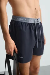 Bañador de hombre azul marino con cintura elástica gris y cordón ajustable. Presenta un pequeño texto estampado en relieve en la parte inferior izquierda.