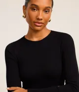 Vestido corto negro de viscosa con mangas largas, cuello redondo y falda godê con superposición de volantes. La parte superior es acanalada y la inferior tiene capas fruncidas.