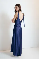 Vestido midi satinado color marrón, con escote en V y tirantes anchos ajustables con lazada en los hombros. Presenta cierre lateral con cremallera oculta.